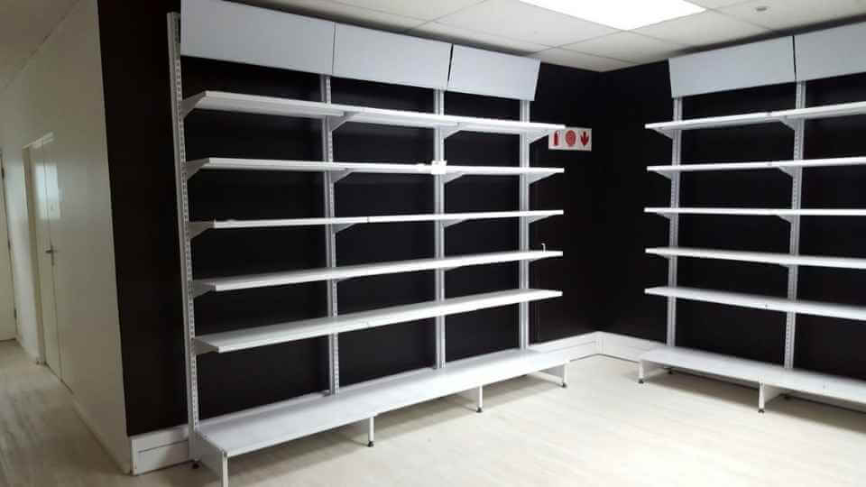 A corner view of a room with empty white metal shelving units against black walls, provided by Duzi Storage Solutions.